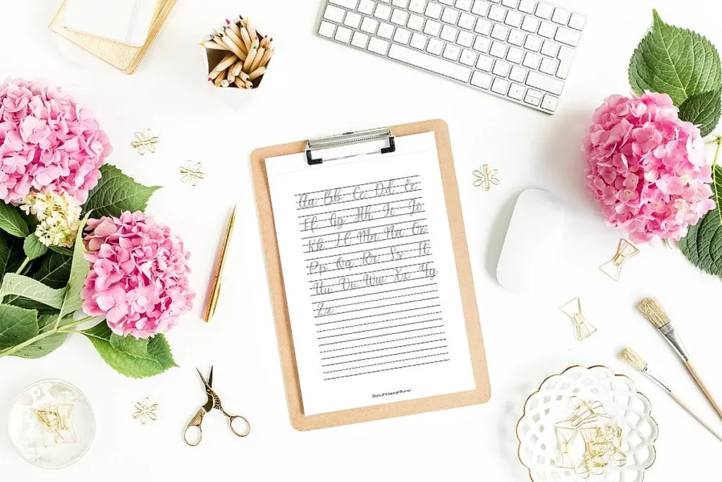 Elegant workspace with pink flowers, calligraphy on clipboard, and desk accessories for a creative and inspiring setup.