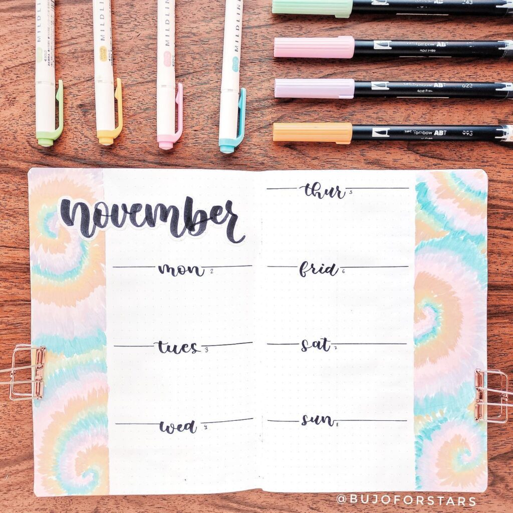 November bullet journal spread with pastel pens and tie-dye theme on wooden table.
