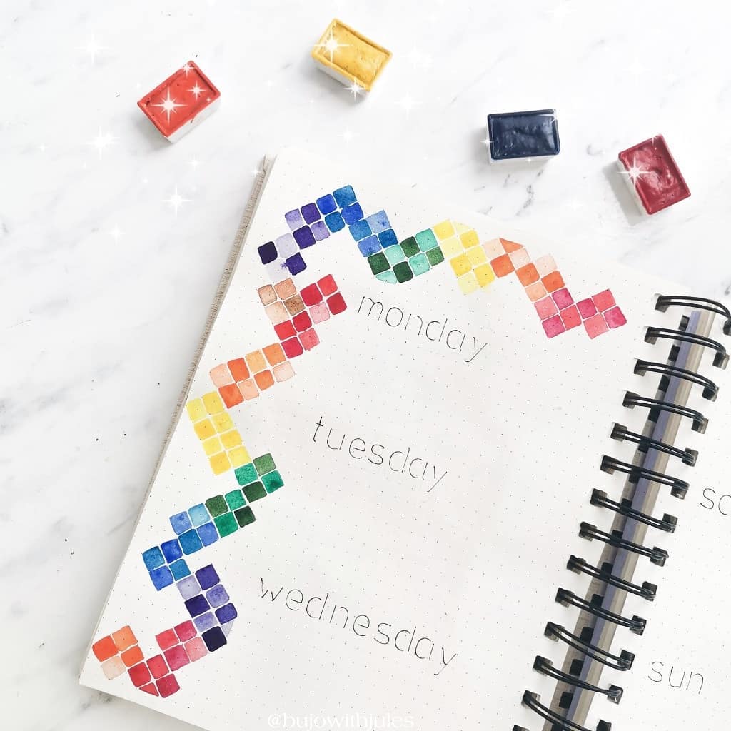 Colorful bullet journal layout with watercolor tiles for Monday to Wednesday on a spiral notebook.