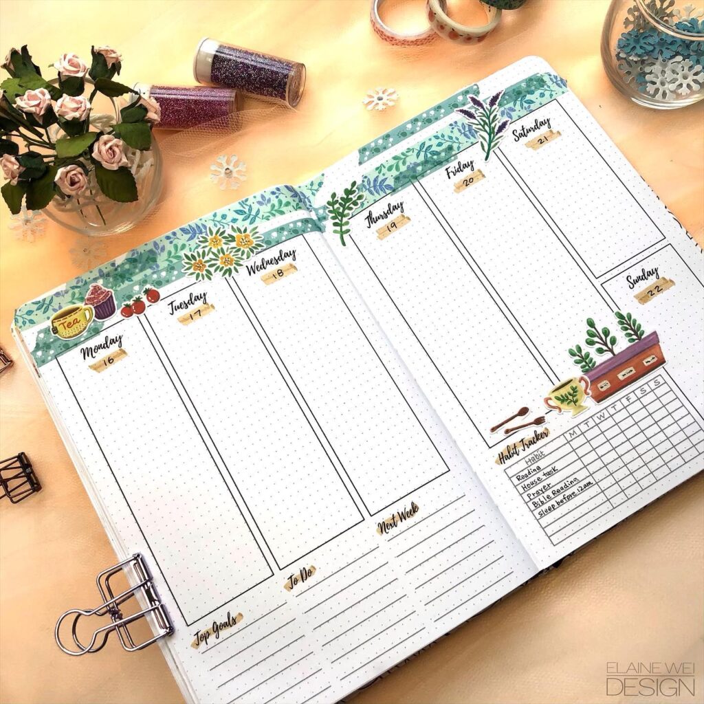 Decorative weekly planner with floral designs, habit tracker, and goal-setting sections on a desk with flowers and glitter.