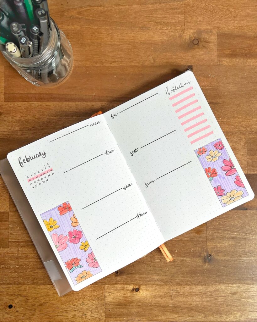 Weekly planner with floral designs and a calendar for February on a wooden desk with pens.
