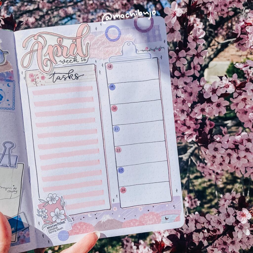 Handwritten bullet journal for April with task list, against a backdrop of blooming pink cherry blossoms.