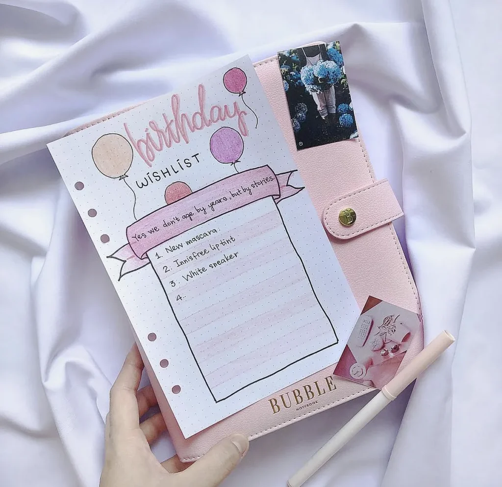 Birthday wishlist on a polka dot paper with a pink planner and pen on a white fabric background.