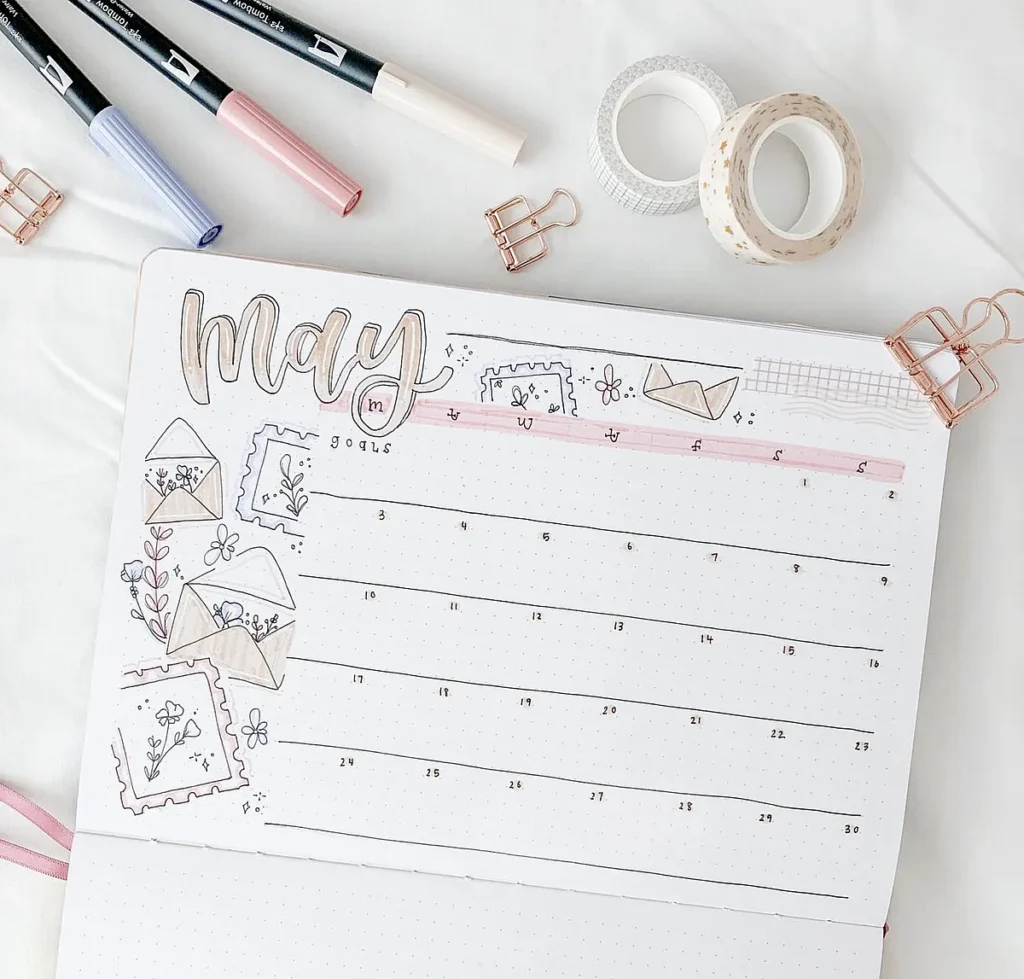 Bullet journal page for May, decorated with markers, washi tape, and floral illustrations. Creative planner setup.