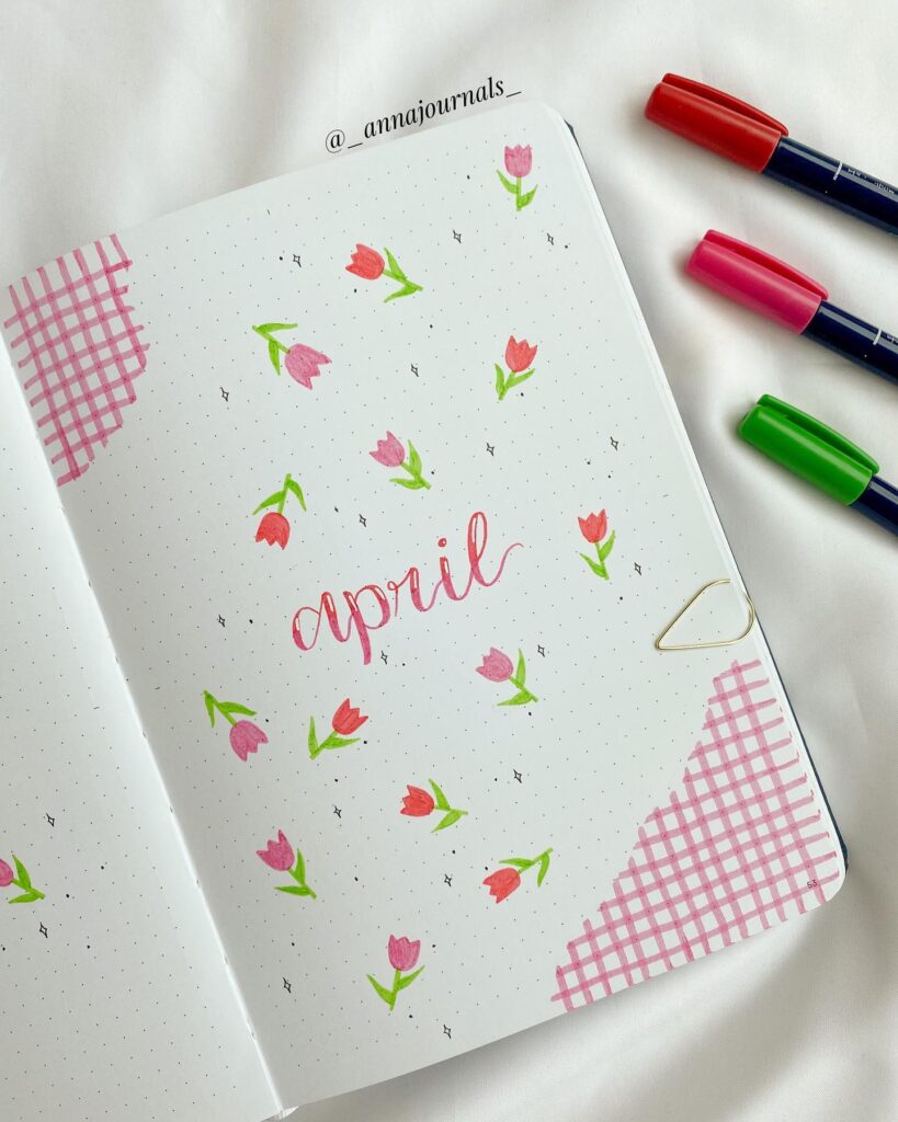 Bullet journal page for April with pink flowers and pens on a white background.