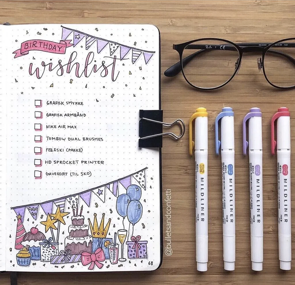 Decorative birthday wishlist journal page with checklist, pens, and glasses on a wooden table.