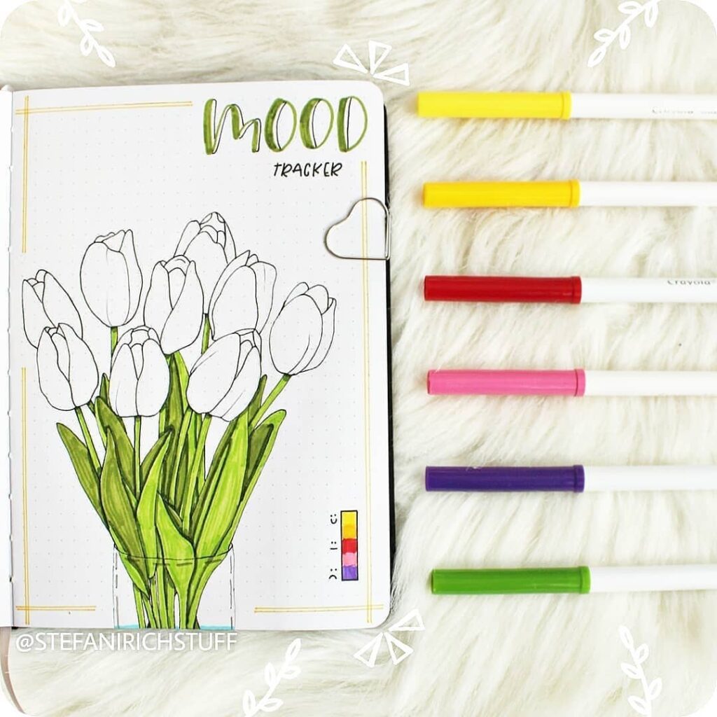 Mood tracker bullet journal with tulip drawing and colorful markers on white fur background.