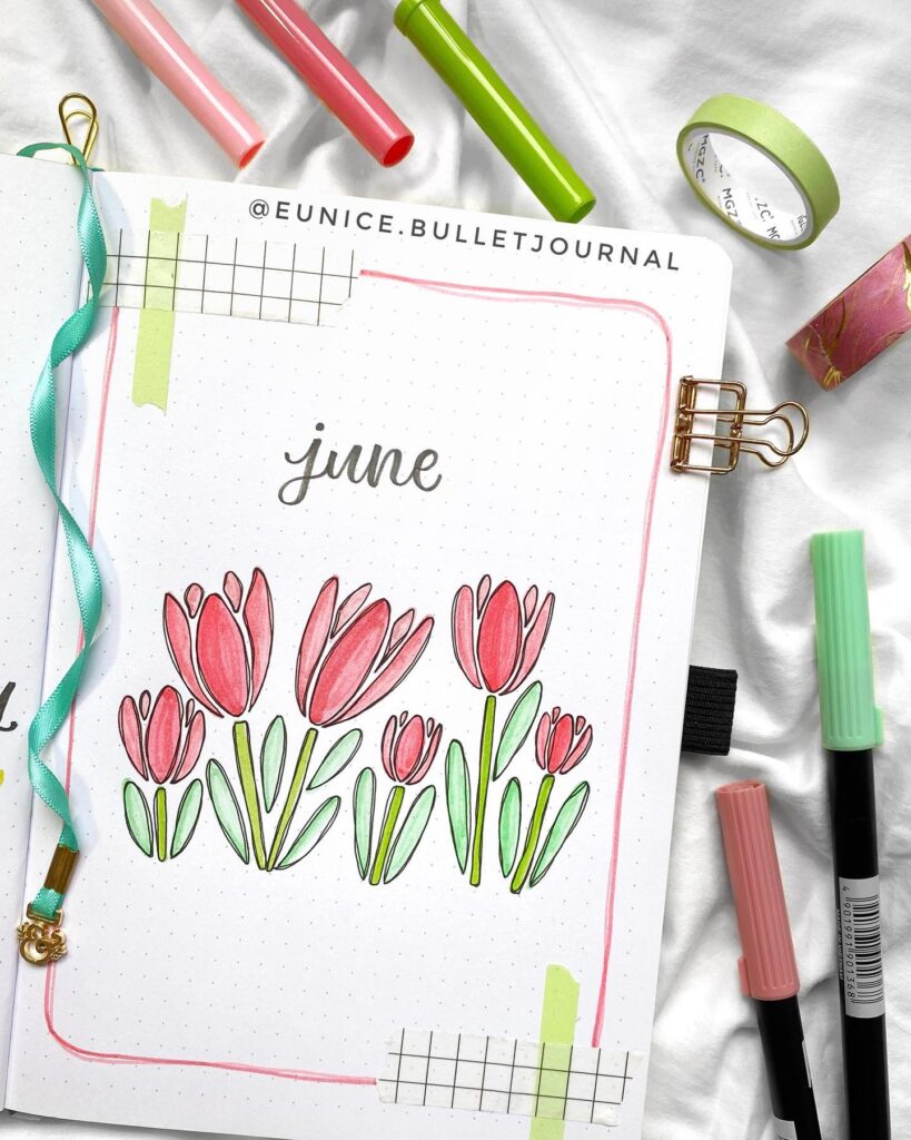 Bullet journal June cover with pink tulips, surrounded by colorful pens and tape.