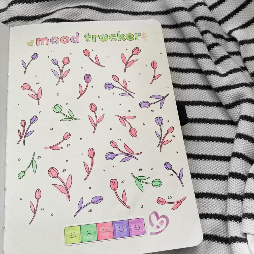Bullet journal mood tracker page with colorful flower doodles on striped fabric background.