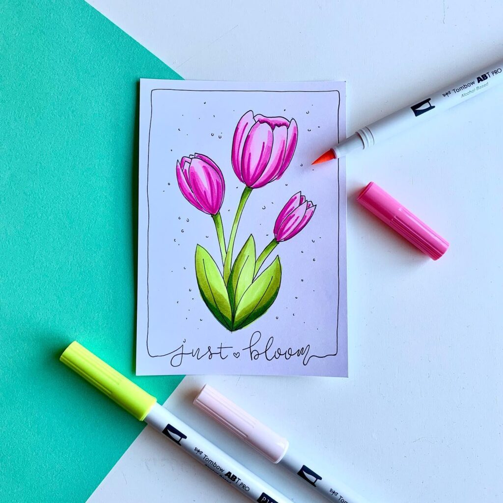 Illustrated pink tulips with just bloom text, surrounded by colorful markers on a teal and white background.