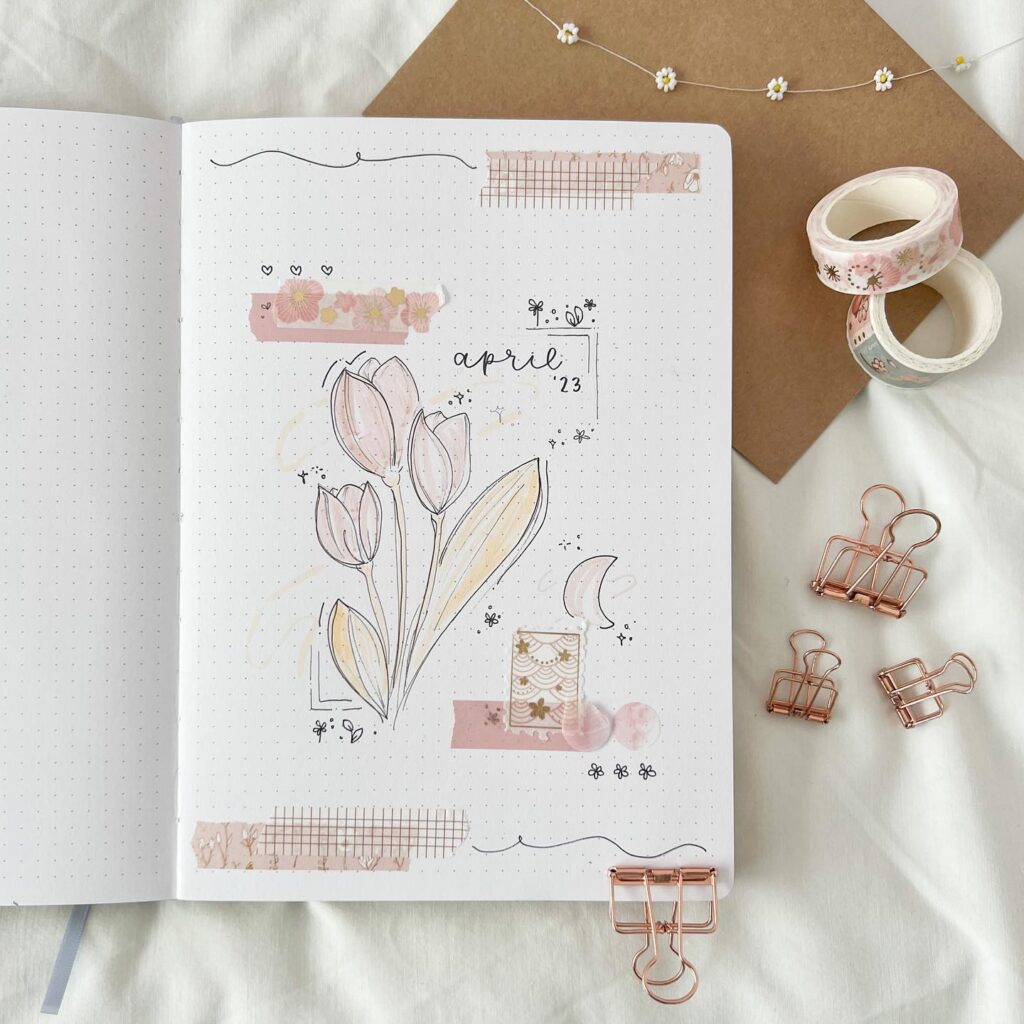 Bullet journal April 2023 layout with floral art, pink washi tape, binder clips, and decorative elements.