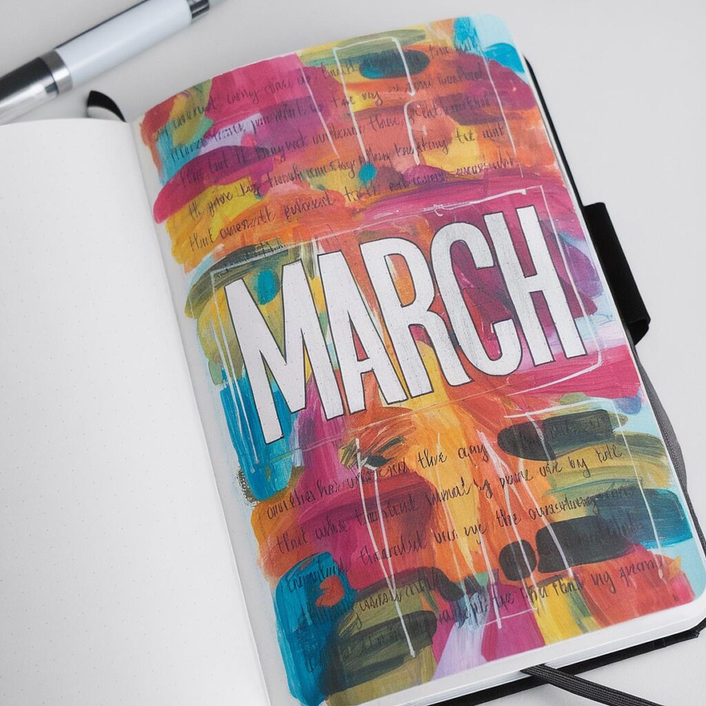 Colorful journal page with March text, artistic background, and pen on a white desk.