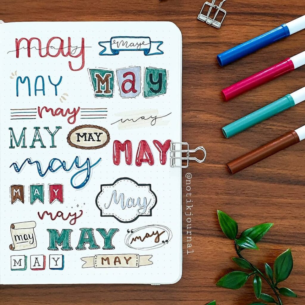 Creative bullet journal page with various May designs and colorful markers on a wooden desk.