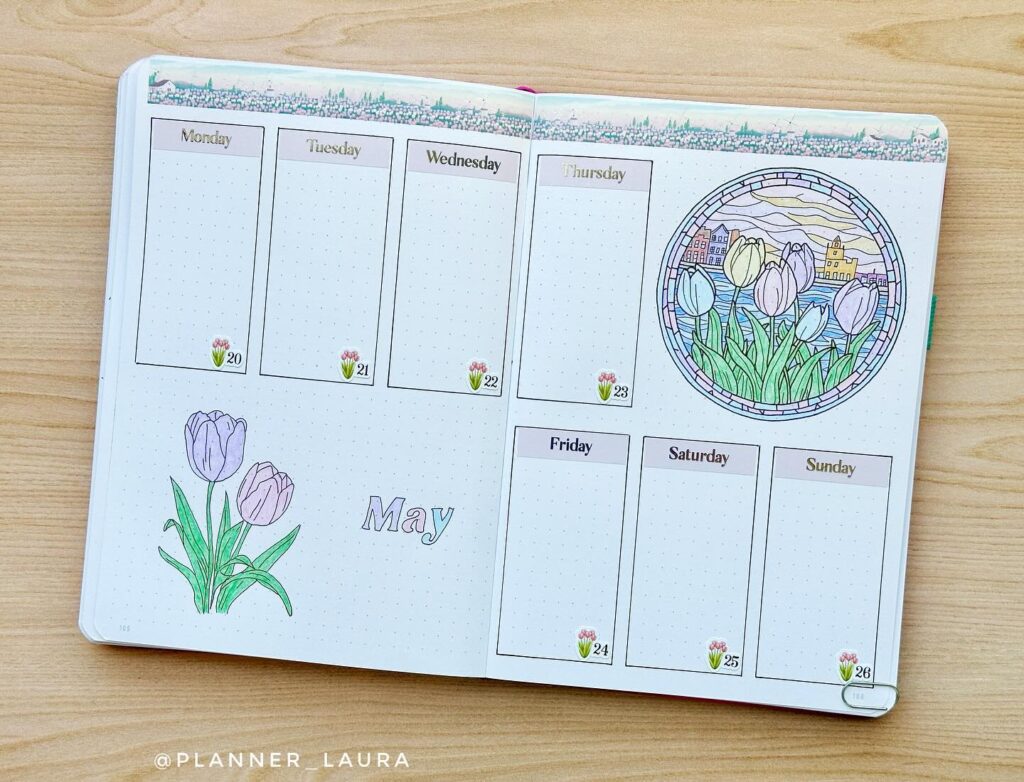 Planner open to May week with tulip illustrations, stained glass art, and calendar layout on a wooden table.