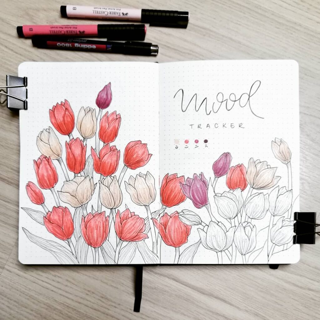 Bullet journal mood tracker with colorful tulip drawings and markers on a wooden desk.