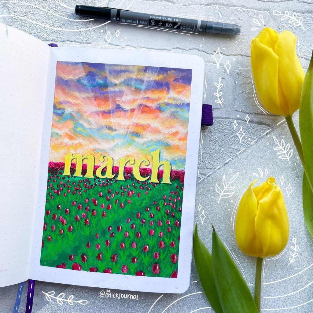 Bullet journal with March cover art featuring a colorful sky and tulip field, surrounded by yellow tulips and a pen.