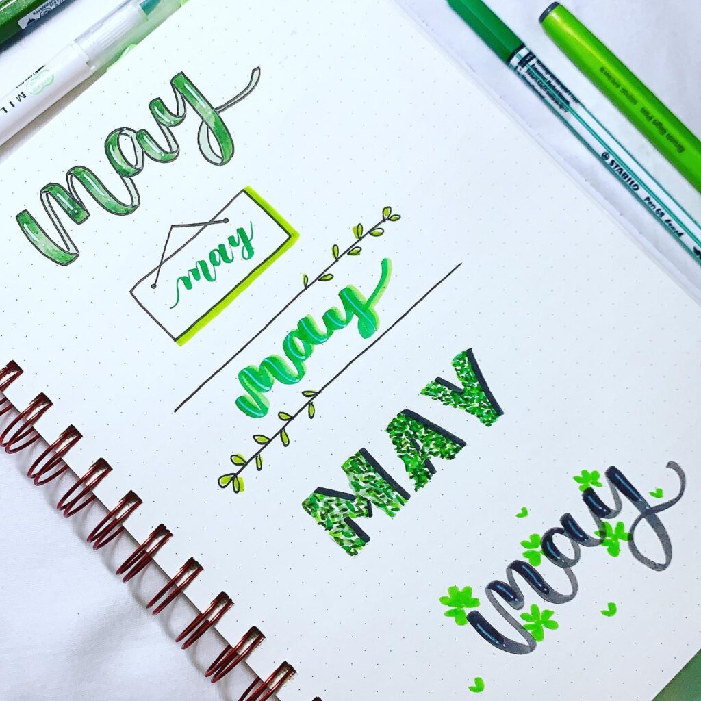 Creative handwritten designs of the word May in green on a dotted notebook page.