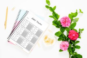Habit tracker journal with pink flowers, gold paper clips, and pen on a white background for planning and productivity.