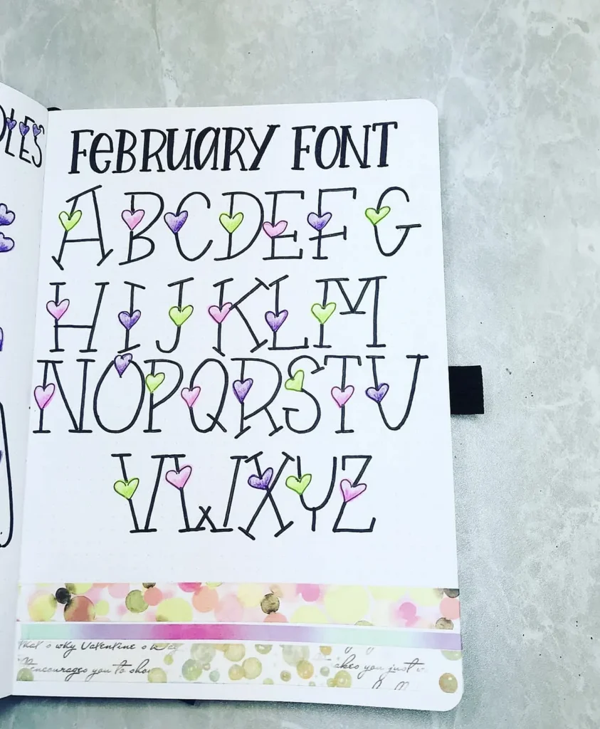 Whimsical February font alphabet with colorful heart accents in a notebook on a textured surface.