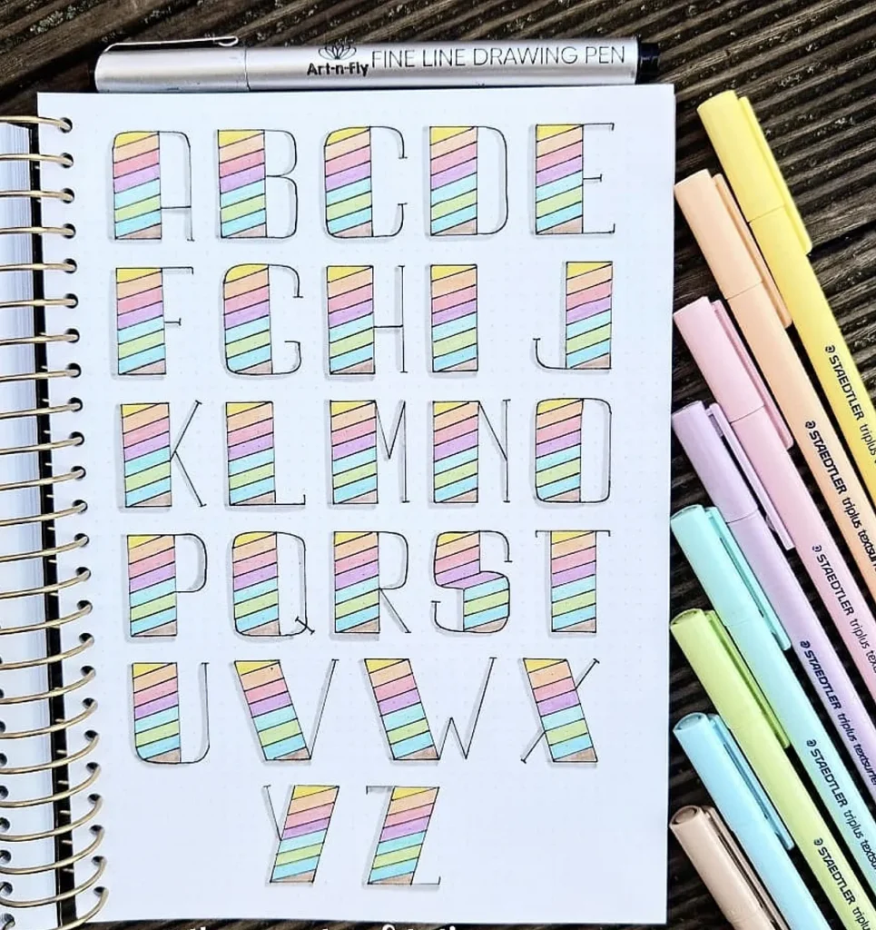Alphabet in pastel colors drawn with markers in a notebook, accompanied by fine line drawing pen and markers.