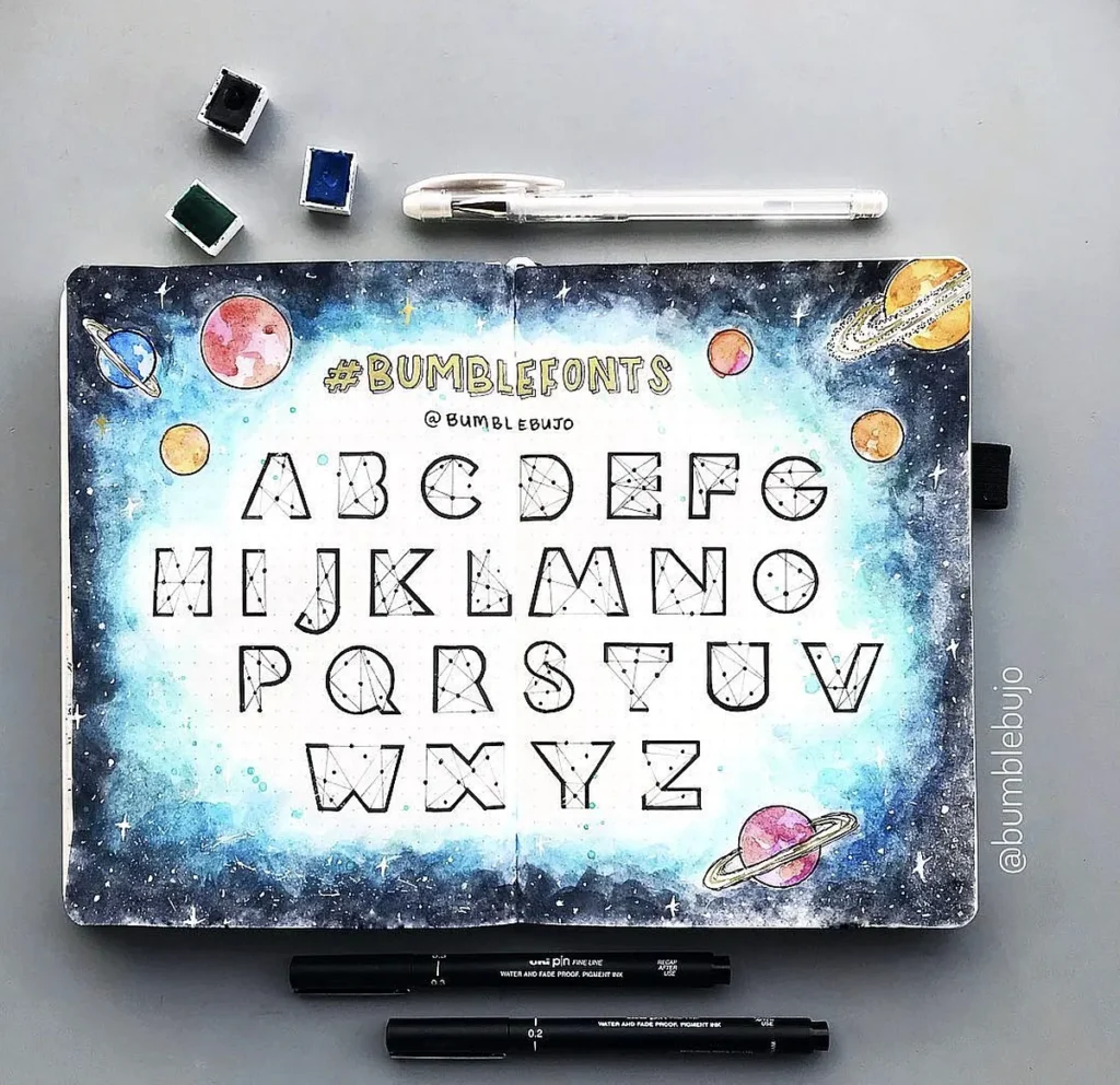 Bullet journal alphabet with galaxy theme and watercolor background, featuring uppercase letters and planets.