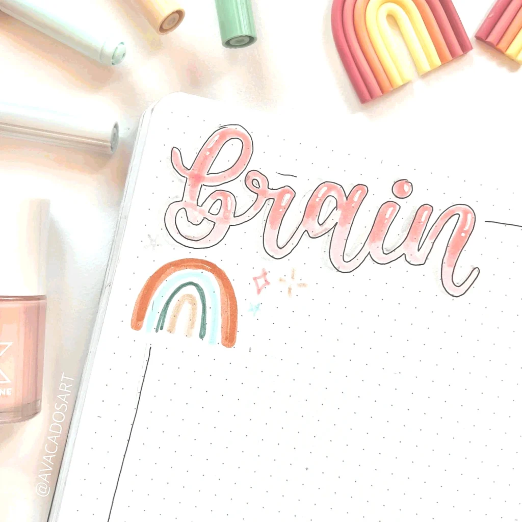 Colorful journal page with brain lettering and rainbow art, surrounded by pastel markers and nail polish.