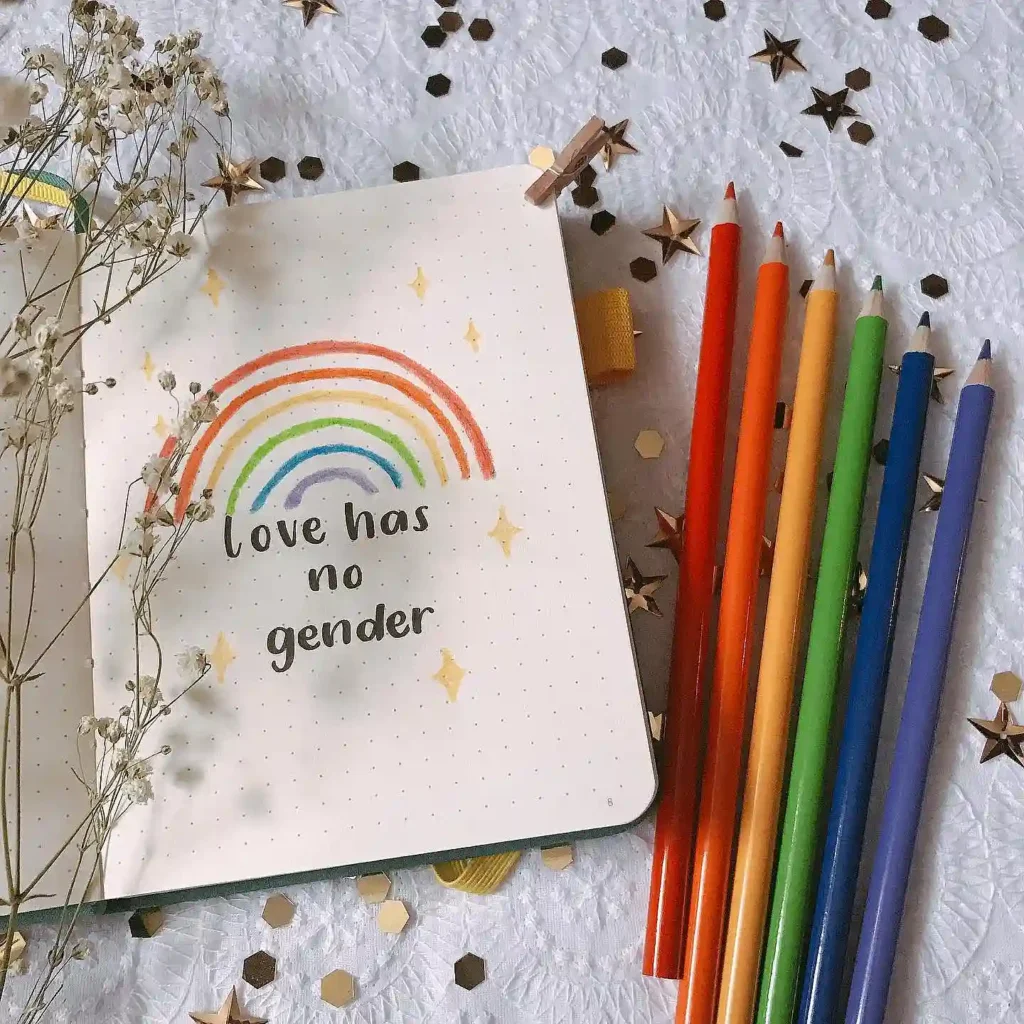 Notebook page with love has no gender under a rainbow, next to rainbow-colored pencils and decorative stars.