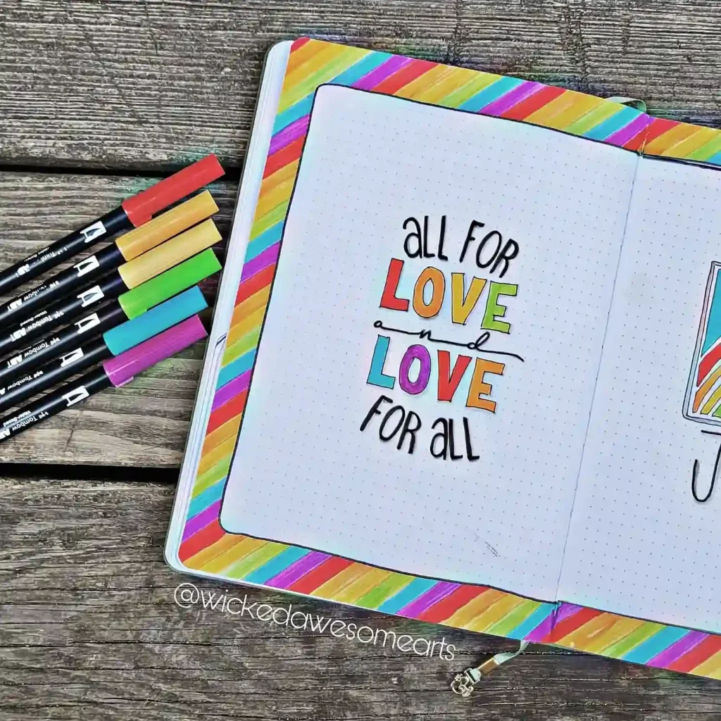 Colorful bullet journal page with All for love and love for all text, featuring rainbow markers on a wooden background.