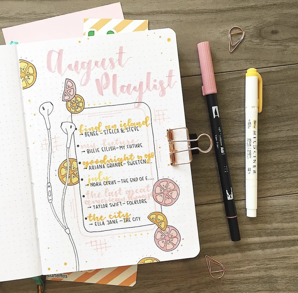 Notebook with August playlist, earbuds, and pens on a wooden table. Decorative lemon slices adorn the page.
