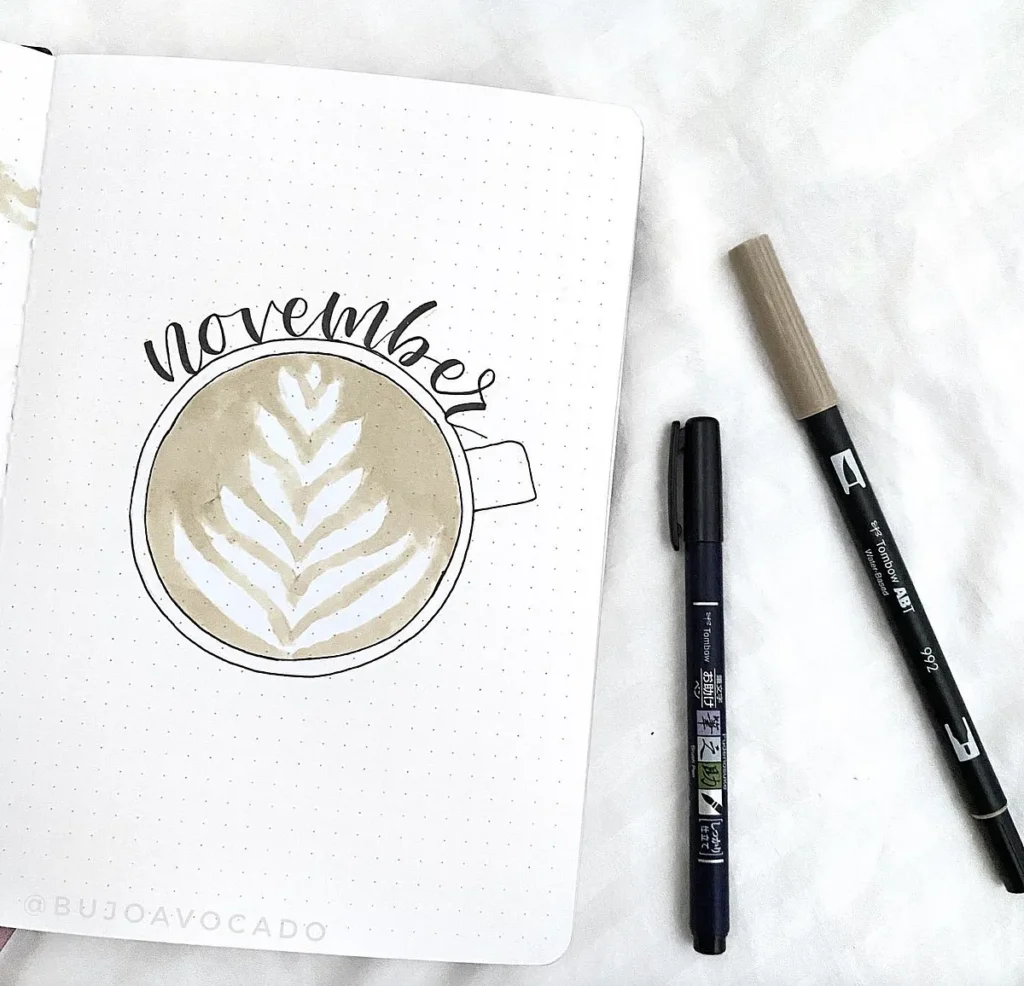 November bullet journal cover with coffee cup illustration and pens on a dotted page.