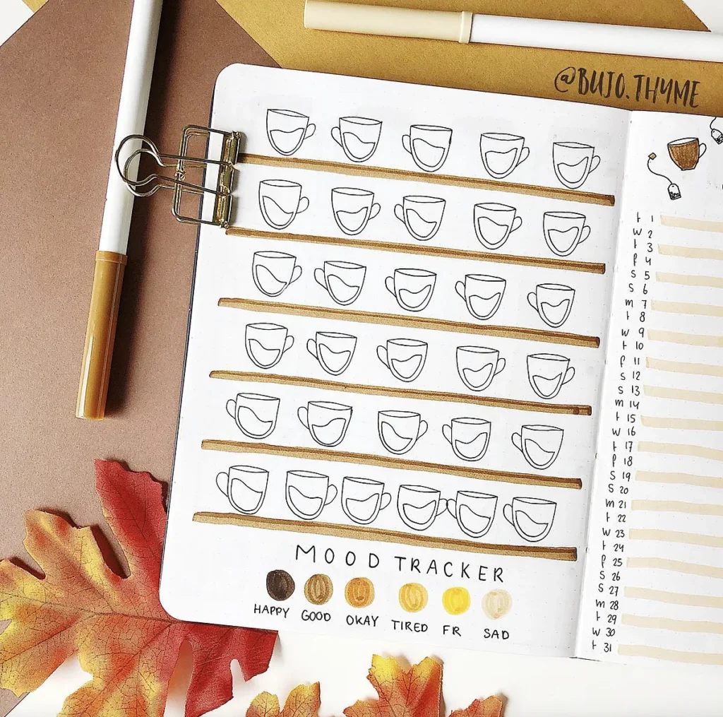 Autumn-themed mood tracker with coffee cup icons, colored for different emotions. Pens and leaves decorate the page.