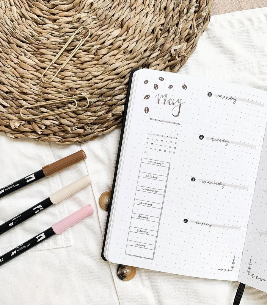 Bullet journal open to May weekly spread with markers and woven mat, ideal for planning and organization.
