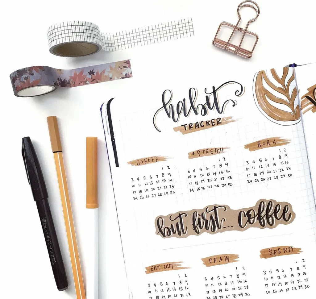 Bullet journal habit tracker with pens, washi tape, and binder clip for organizing daily routines.