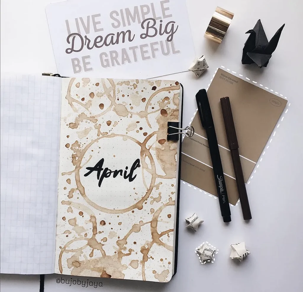 Bullet journal with April theme, surrounded by pens, origami, and an inspirational quote card.