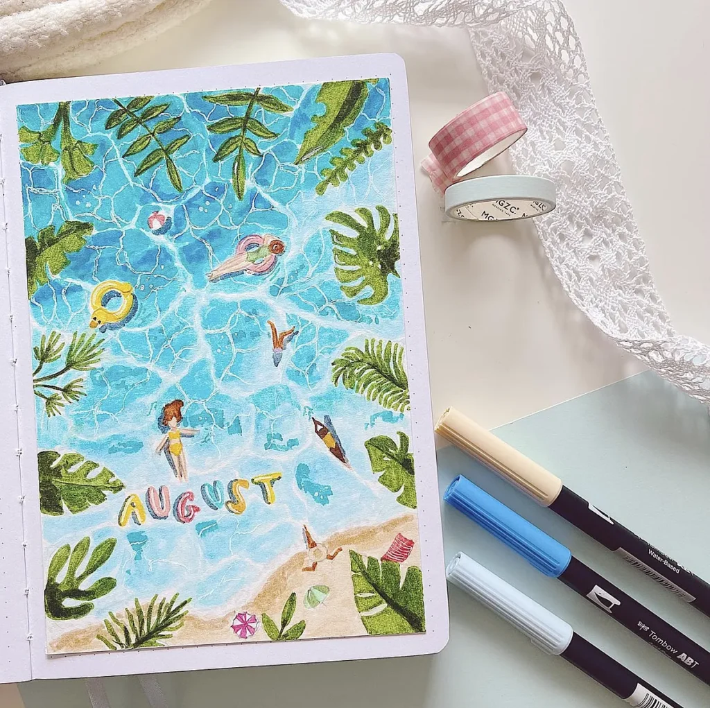 Illustrated August-themed journal page with a beach, leaves, and pool motifs, surrounded by art supplies on a desk.