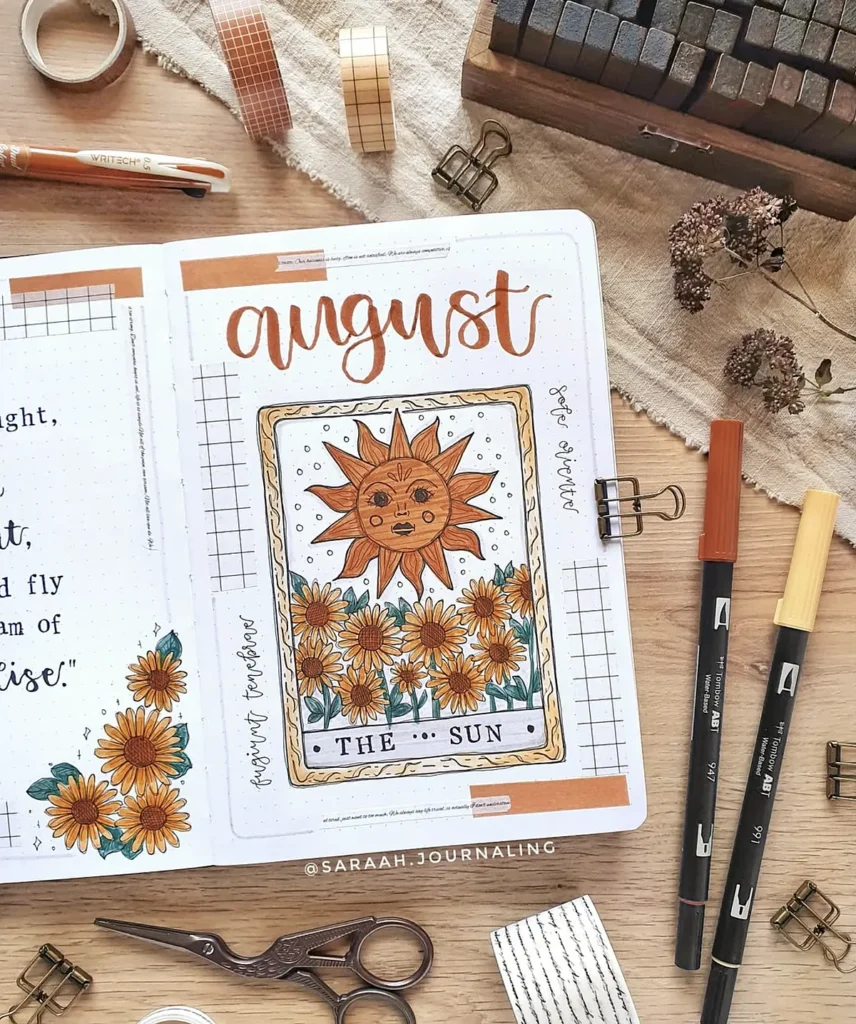 August bullet journal page with sun tarot card and sunflower theme, surrounded by pens and stationary items.
