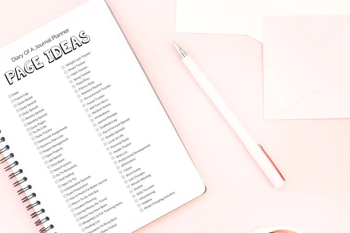 Open journal with bullet journal page ideas list, pink pen, and envelope on a pastel pink background. Perfect for planning inspiration.