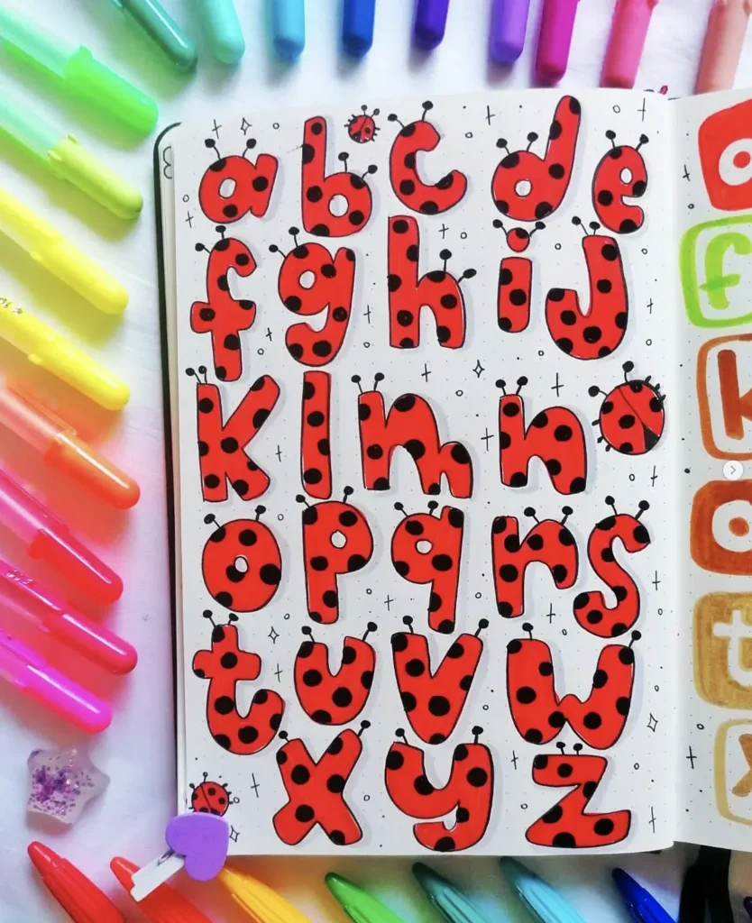 Alphabet letters styled as ladybugs surrounded by colorful markers on a notebook page. Creative bullet journal idea.