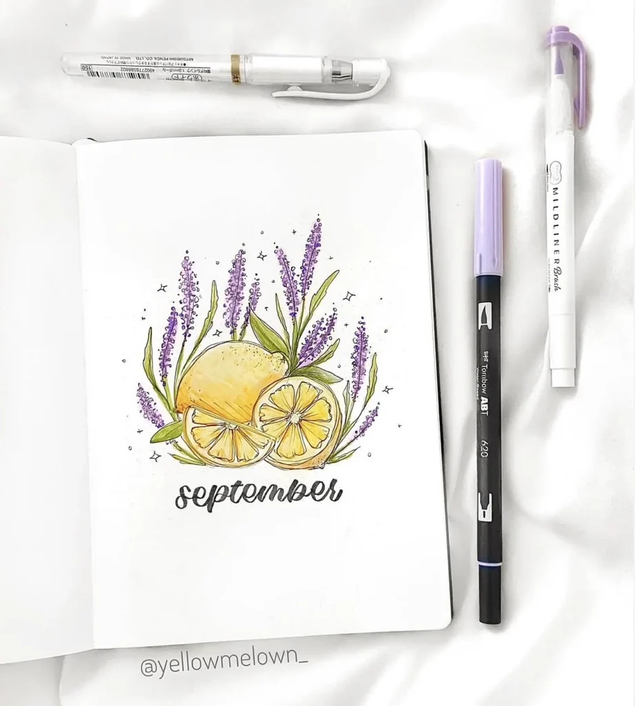 Hand-drawn September calendar with lemons and lavender on open notebook, surrounded by pens and markers.