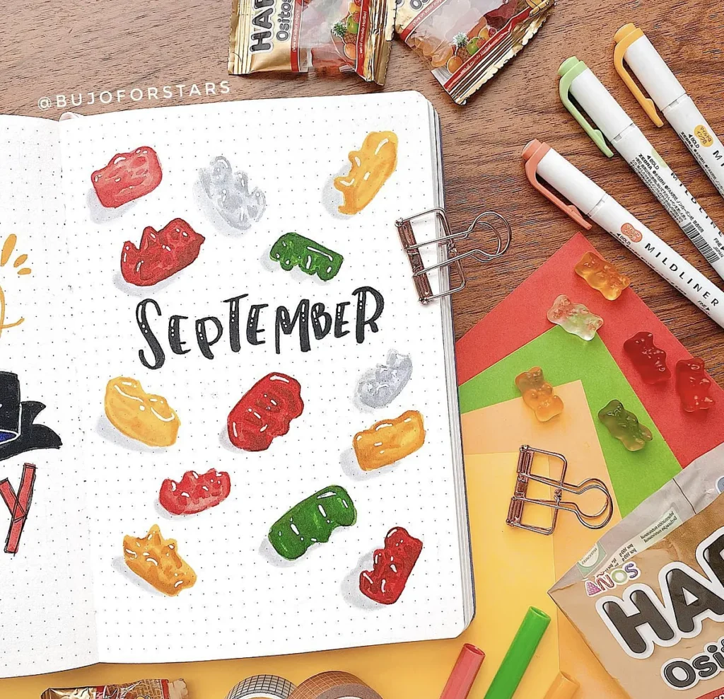 Bullet journal page for September with colorful gummy bears, pens, and stationery on a wooden desk background.