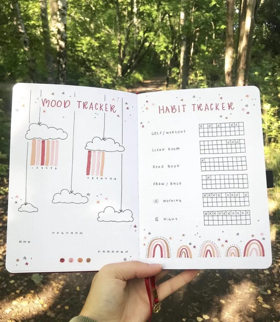 Open journal with mood and habit trackers, featuring colorful designs, held in a lush green forest setting.
