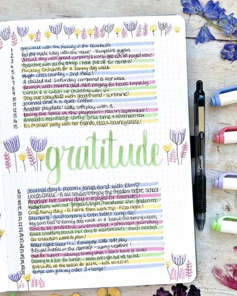Decorative gratitude journal page with colorful entries and floral designs, surrounded by pens and dried flowers.