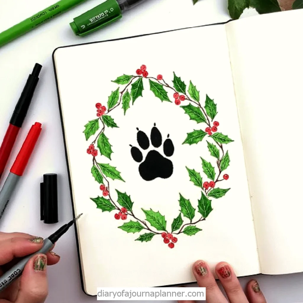 Artistic paw print surrounded by a wreath of holly leaves and berries in a journal, with colorful markers around.
