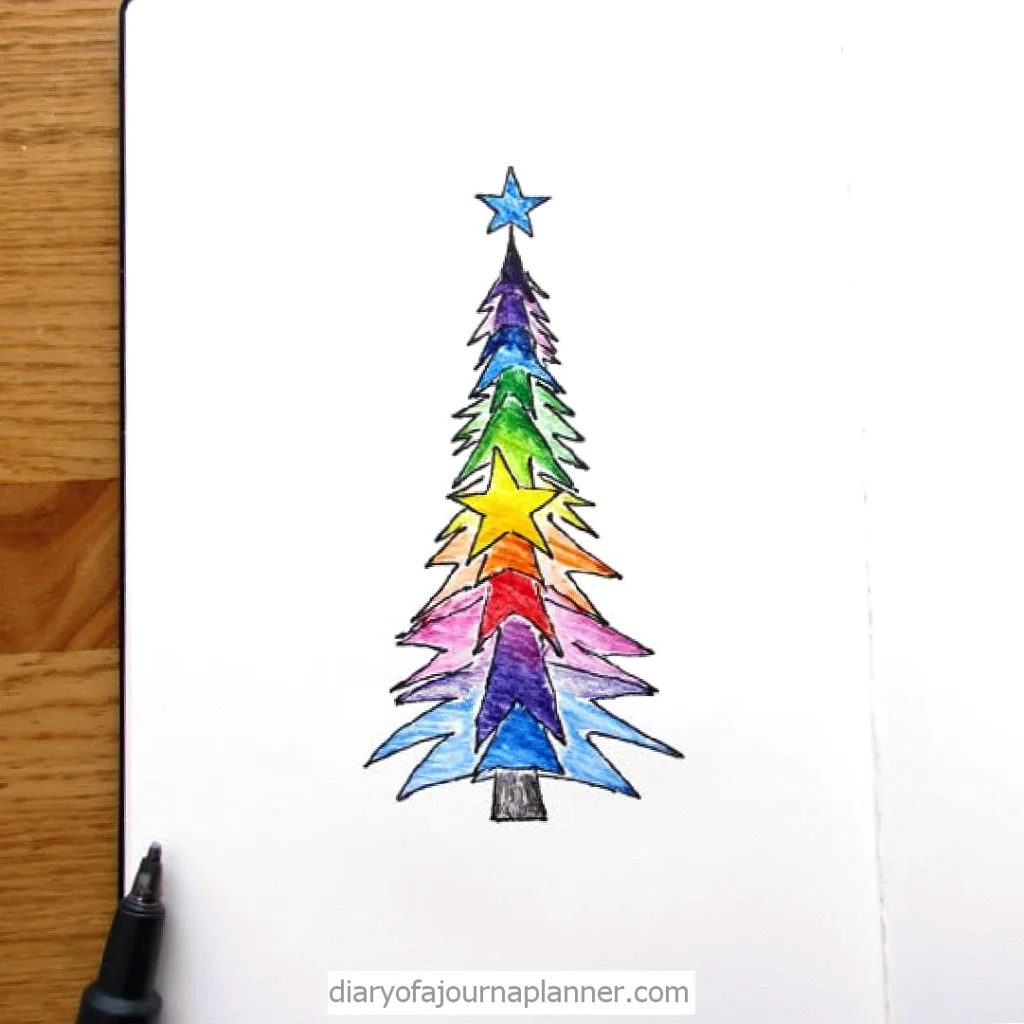 Colorful hand-drawn Christmas tree with star layers, notebook and pen on wooden table background.