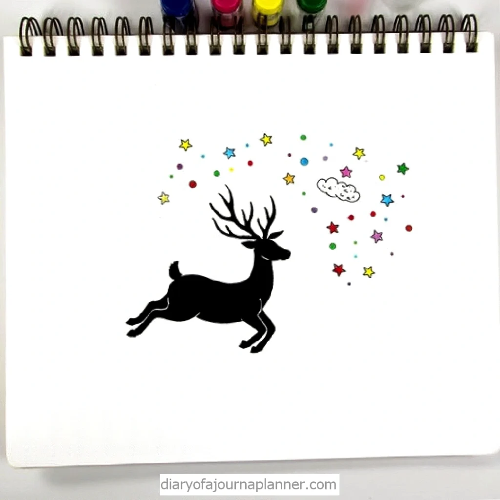 Silhouette of a leaping reindeer among colorful stars and a cloud on a sketchbook with markers on top.