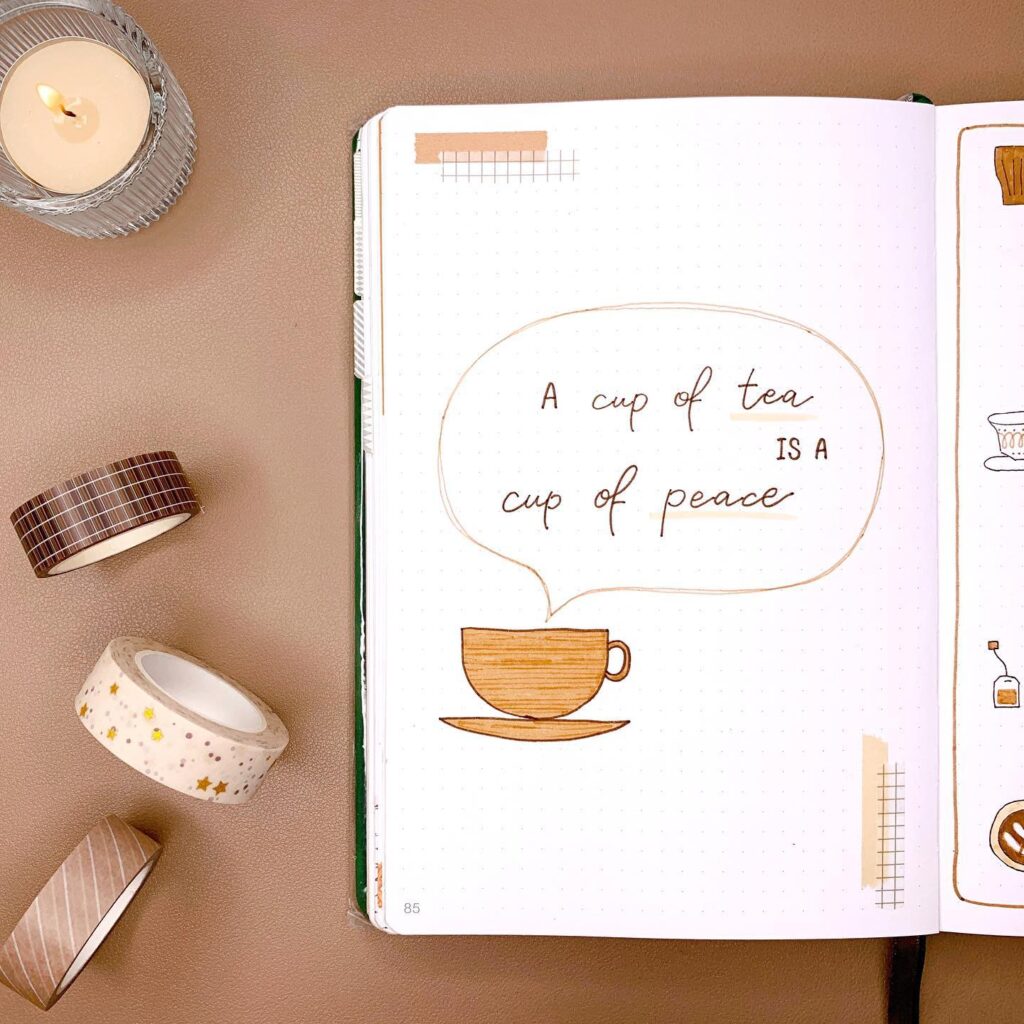 Open journal with quote A cup of tea is a cup of peace, surrounded by decorative tape and a lit candle.