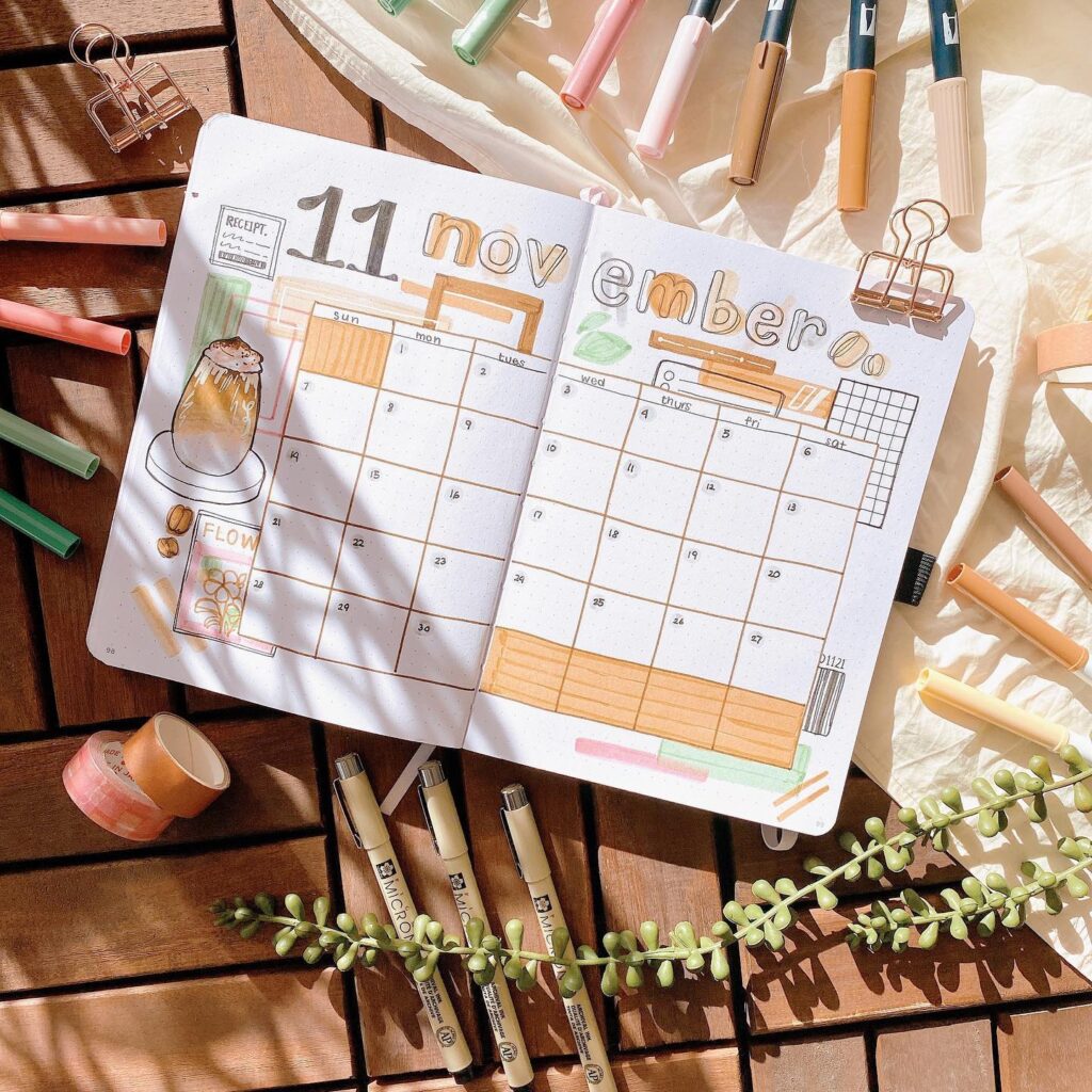 Hand-drawn November bullet journal spread with colorful pens on wooden table.