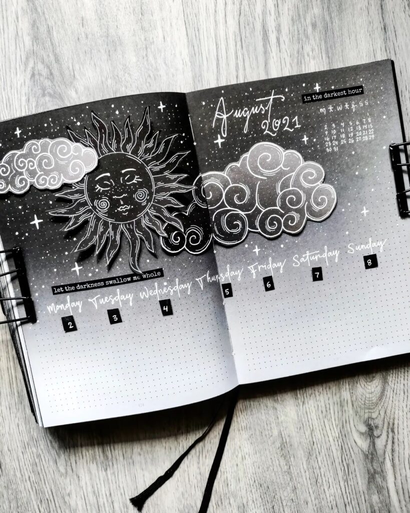 Black and white bullet journal spread for August 2021 with celestial sun and cloud illustrations.