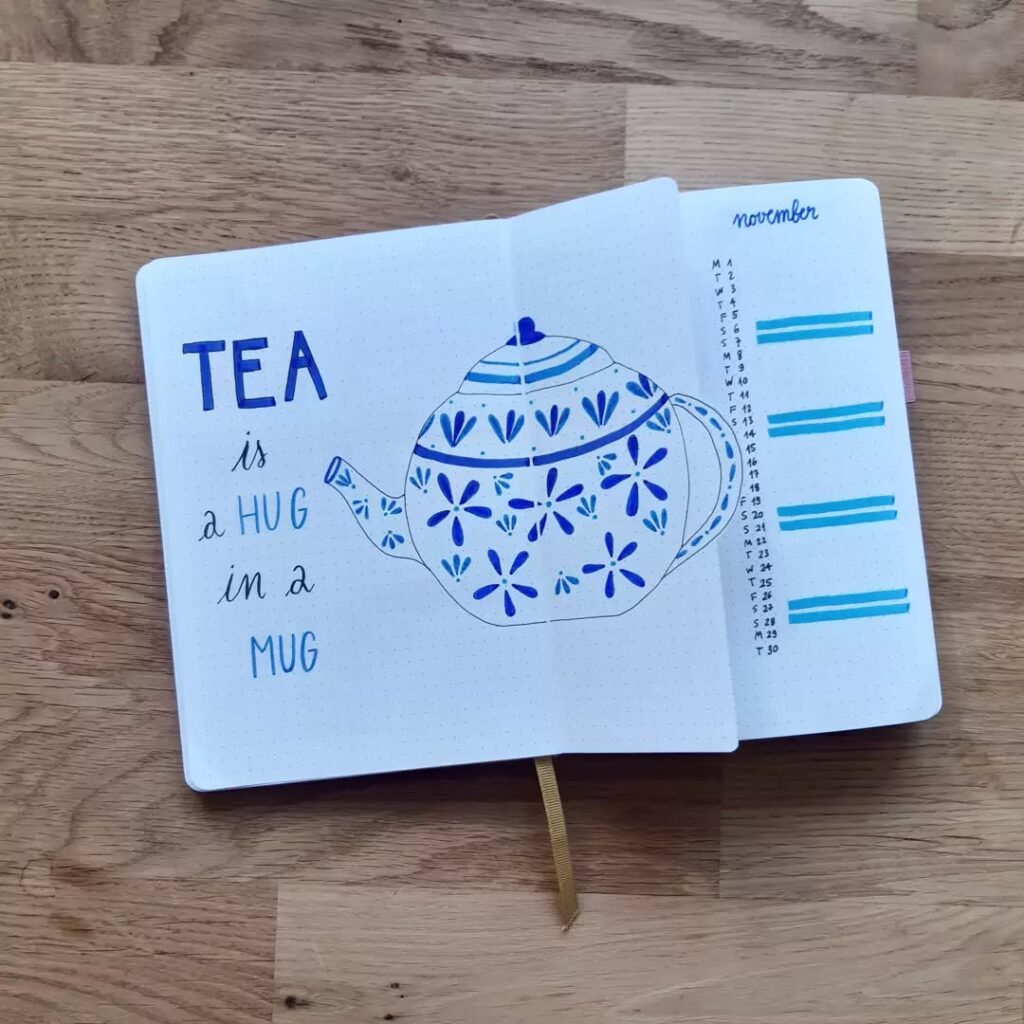Open journal with blue teapot drawing and quote, Tea is a hug in a mug, alongside a November calendar layout.