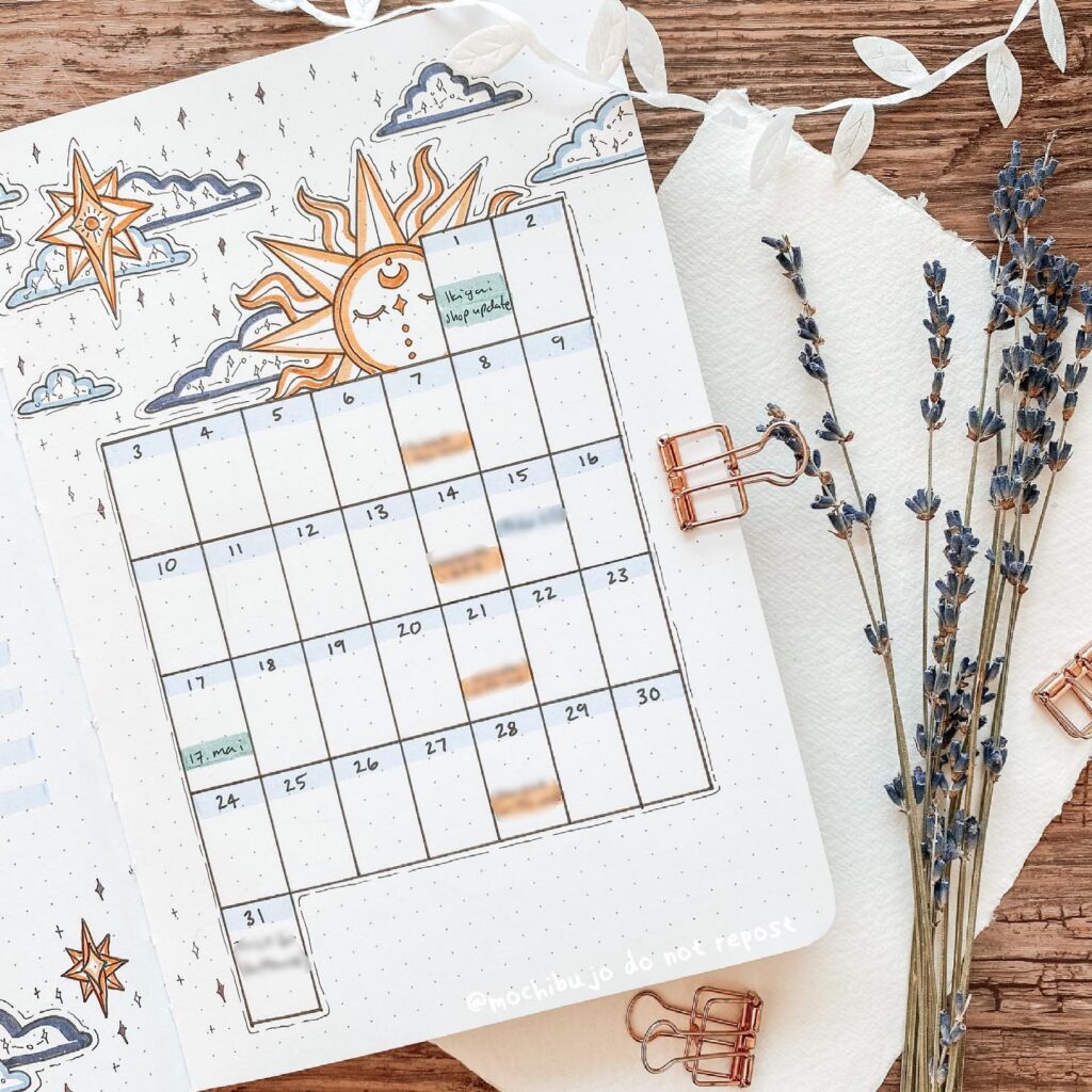 Decorative bullet journal layout with calendar, sun and cloud doodles, lavender sprigs, and copper paper clips.